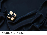 Black Friday concept. Sale of goods at reduced prices. Eco-friendly craft paper gift box with black bow on black silk fabric background. Gifts for men. Flat lay, copy space, blank, close-up, top view, mock up. Стоковое фото, фотограф Виктория Катьянова / Фотобанк Лори