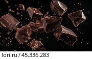 Dark chocolate pieces splintering in mid-air against a black background during a culinary demonstration. Стоковое AI-изображение, AI-художник Сергей Толмачёв / Фотобанк Лори