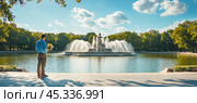 Man holding flowers admiring james scott memorial fountain in belle isle park detroit. Стоковое AI-изображение, AI-художник Юрий Поздников / Фотобанк Лори