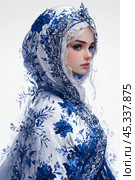 Elegant young woman in intricately designed blue and white headscarf adorned with floral patterns showcasing cultural beauty. Стоковое AI-изображение, AI-художник Елена Зубкова / Фотобанк Лори