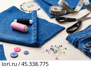 Sewing supplies and denim fabric arranged on a workspace for clothing alterations in a bright setting. Стоковое фото, фотограф Сергей Толмачёв / Фотобанк Лори