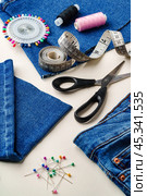 Sewing supplies and denim fabric arranged on a workspace for clothing alterations in a bright setting. Стоковое фото, фотограф Сергей Толмачёв / Фотобанк Лори