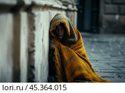 Homeless person wrapped in an old blanket sitting against a wall on a city street. concept of deprivation, vagrancy, homelessness. Стоковое AI-изображение, AI-художник 123 12 / Фотобанк Лори