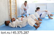 Multinational group of focused teenagers in white kimono performing core twist exercise with simultaneous punches during martial arts training session under guidance of experienced adult coach. Стоковое видео, видеограф Яков Филимонов / Фотобанк Лори