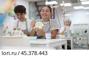 Young couple joyfully talking and working together on ceramic pottery, enjoying creative process while painting mugs in light workshop. Стоковое видео, видеограф Яков Филимонов / Фотобанк Лори