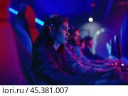 Female pro gamer competes intensely in an esports tournament, surrounded by teammates. Стоковое AI-изображение, AI-художник Arsenii Palivoda / Фотобанк Лори
