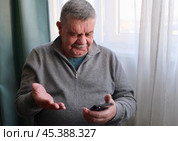 Смартфон в руках у пенсионера. Пожилой мужчина читает сообщения по смартфону и удивляется. Стоковое фото, фотограф Терехова Марина / Фотобанк Лори