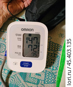 Цифровой тонометр на столе рядом с рукой пожилого человека. A digital blood pressure monitor on the table next to an elderly man's hand. Редакционное фото, фотограф Дарья Жихарева / Фотобанк Лори