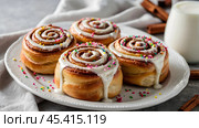 The cinnabons. Close-up of cinnamon buns. Beautiful buns with fresh cinnamon and icing on a wooden table. Fragrant homemade New Year's pastries. Стоковое AI-изображение, AI-художник Photojuli / Фотобанк Лори