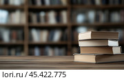 Стопка книг лежит на деревянном столе в библиотеке, на заднем плане видна размытая книжная полка, символизирующая знания, обучение и стремление к образованию. Стоковое AI-изображение, AI-художник ФотоИнтеллект / Фотобанк Лори