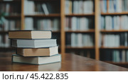 Стопка книг на столе в библиотеке с размытой книжной полкой. Стоковое AI-изображение, AI-художник ФотоИнтеллект / Фотобанк Лори