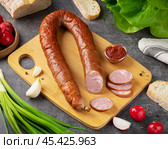 Delicious traditional sausage displayed on a wooden cutting board with fresh vegetables and bread in a rustic kitchen setting. Стоковое фото, фотограф Евгения Трушкова / Фотобанк Лори