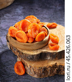 Dried apricots arranged in a rustic wooden bowl on a wooden slab in natural lighting captured indoors. Стоковое фото, фотограф Евгения Трушкова / Фотобанк Лори