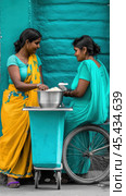 Two women in vibrant saris share a meal by a teal wall, AI. Стоковое AI-изображение, AI-художник Сергей Старуш / Фотобанк Лори