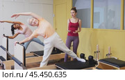 Senior woman doing exercises on reformer in pilates studio with young female personal trainer controlling her movements. Стоковое видео, видеограф Яков Филимонов / Фотобанк Лори