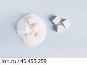 Lump sugar on a pile of granulated sugar and next to it on a blue background, top view. Стоковое фото, фотограф Елена Руй / Фотобанк Лори