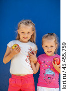 Two little girls posing with two ripe apples against blue wall. Стоковое фото, фотограф Андрей Аркуша / Фотобанк Лори