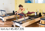 Young woman doing pilates exercises with reformer bed. Стоковое фото, фотограф Яков Филимонов / Фотобанк Лори