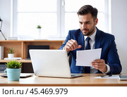 A businessman is working on a laptop with documents. Стоковое AI-изображение, AI-художник RamA / Фотобанк Лори