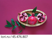 Top view of ripe pomegranates and pomegranate tree leaves on a wooden plate on burgundy background. Beautiful still life. Natural organic seasonal fruits with healthy vitamins. Flat lay, copy space. Стоковое фото, фотограф Виктория Катьянова / Фотобанк Лори