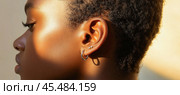 Model showing stylish earrings and highlighter makeup in golden light. Стоковое AI-изображение, AI-художник Юрий Поздников / Фотобанк Лори