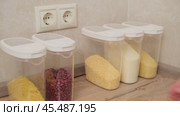 Hand arranging plastic containers with grains and cereals on a wooden kitchen countertop. Kitchen storage organization concept. Стоковое видео, видеограф Андрей Журавлев / Фотобанк Лори
