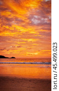 Beautiful peaceful romantic evening sunset landscape on tropical sandy beach with sea waves, reflection and bright yellow and orange dramatic clouds with sunlight for relaxation and rest on vacations. Стоковое фото, фотограф Елена Кабенкина / Фотобанк Лори