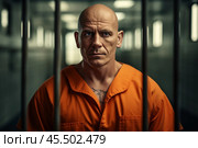 A prisoner in an aged orange uniform stares intently at the camera from behind metal bars, capturing the gravity of incarceration. The setting is a dimly lit detention center. Стоковое AI-изображение, AI-художник Sergey Grishin / Фотобанк Лори