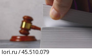 A man quickly flips through a thick book against the background of a judge's gavel, close-up, searching for information. Стоковое видео, видеограф Сергей Чайко / Фотобанк Лори