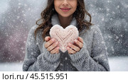 Women's hands in warm mittens hold a pink heart. Snow is falling. Valentine's Day and World Health, Love and Family Insurance Day. Стоковое AI-изображение, AI-художник Photojuli / Фотобанк Лори
