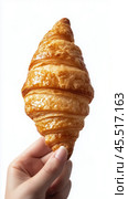 Hand holding a freshly baked croissant with golden layers in a minimalistic setting. Стоковое AI-изображение, AI-художник Юлия Гапеенко / Фотобанк Лори