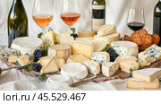 Cheese board displaying variety of cheeses with wine and crackers. Стоковое AI-изображение, AI-художник Юрий Поздников / Фотобанк Лори