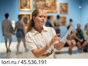 Young girl holding an information booklet looks at paintings in an art exhibition in museum. Стоковое фото, фотограф Яков Филимонов / Фотобанк Лори