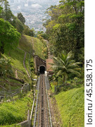 Penang Hill funicular railway in Malaysia, moving down hillside, surrounded by dense tropical forest. Offers panoramic views of lush greenery and city skyline in distance. must-visit spot for tourists. Стоковое фото, фотограф Павел Муравьев / Фотобанк Лори