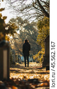 Woman paying respects at cemetery on sunny autumn day. Стоковое AI-изображение, AI-художник Юрий Поздников / Фотобанк Лори