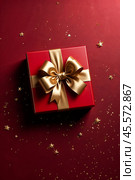 Perfect red Christmas present gift box with elegant gold bow ribbon on red background near stars. Greeting gift symbolize lovely holiday gifting. Birthday Christmas festive concept. Copy ad text space. Стоковое AI-изображение, AI-художник Aleksandr Golubev / Фотобанк Лори
