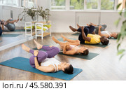 Asian woman performing Pawanmuktasana at group yoga session. Стоковое фото, фотограф Яков Филимонов / Фотобанк Лори