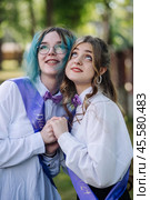 Two jubilant graduates in purple sashes hold hands and gaze hopefully on their final day of school. Стоковое фото, фотограф Mikhail Davidovich / Фотобанк Лори