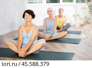 In sport studio with small group of friends, elderly woman performs butterfly pose, Baddha Konasana. Стоковое фото, фотограф Яков Филимонов / Фотобанк Лори