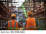 Rear view of workers, wearing helmets and protective west, on a construction site. Стоковое AI-изображение, AI-художник Михаил Строгалев / Фотобанк Лори