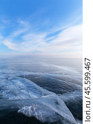 Winter natural blue background of frozen Baikal Lake with ice surface with cracks and blue sky with clouds on cold day. Endless icy expanses to horizon. Scenic winter landscape. Стоковое фото, фотограф Виктория Катьянова / Фотобанк Лори