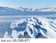 Beautiful winter landscape with snow crust on blue ice surface on frozen Baikal Lake on cold winter sunny day. Snow-covered white mountains and hills on distance. Scenic winter nature background. Стоковое фото, фотограф Виктория Катьянова / Фотобанк Лори