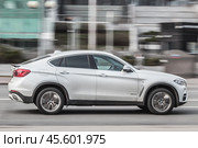 Side view rolling shot with white car in motion. BMW X6 F16 driving along the street in city with blurred background (2021 год). Редакционное фото, фотограф Константин Григорьев / Фотобанк Лори