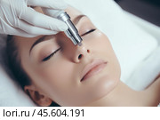 A woman enjoys a hydro microdermabrasion treatment at a cosmetic beauty spa. The procedure uses a specialized device for exfoliation and hydration of her skin, promoting rejuvenation. Стоковое AI-изображение, AI-художник Sergey Grishin / Фотобанк Лори