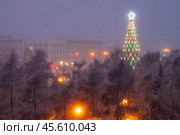 Большая новогодняя ёлка в городском сквере. Зимний городской пейзаж. Красивая рождественская ель, украшенная гирляндами и звездой. Вид сверху на деревья. Холодная погода. Праздничное новогоднее и рождественское настроение. Город Иркутск, Иркутская область, Россия. Редакционное фото, фотограф Андрей Степанов / Фотобанк Лори