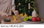Cook cuts cheese into thin slices in order to serve it at Christmas table, which also includes variety of vegetables, fruits, and champagne. Стоковое видео, видеограф Strunov David / Фотобанк Лори