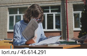 Two high school or university students reviewing their notes and studying together at a table outdoors on a sunny day. Стоковое видео, видеограф Mikhail Davidovich / Фотобанк Лори