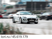 Jaguar F-Type S coupe driving on the street in Moscow. White supercar moving fast in front of blurred city background. Редакционное фото, фотограф Константин Григорьев / Фотобанк Лори