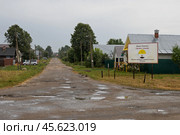 Деревня Среднее Азяково, Республика Марий Эл, Россия. Информационный щит на въезде в деревню с названием деревни Среднее Азяково на русском и марийском языках и текстом «Деревня основана в первой четверти XVI века». Вид на деревенскую улицу. Пасмурная дождливая погода. (2024 год). Редакционное фото, фотограф Андрей Степанов / Фотобанк Лори