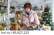 Portrait of adult female buyer with shopping cart or basket holding assortment of cheese choosing for christmas table in grocery shop. Стоковое видео, видеограф Яков Филимонов / Фотобанк Лори
